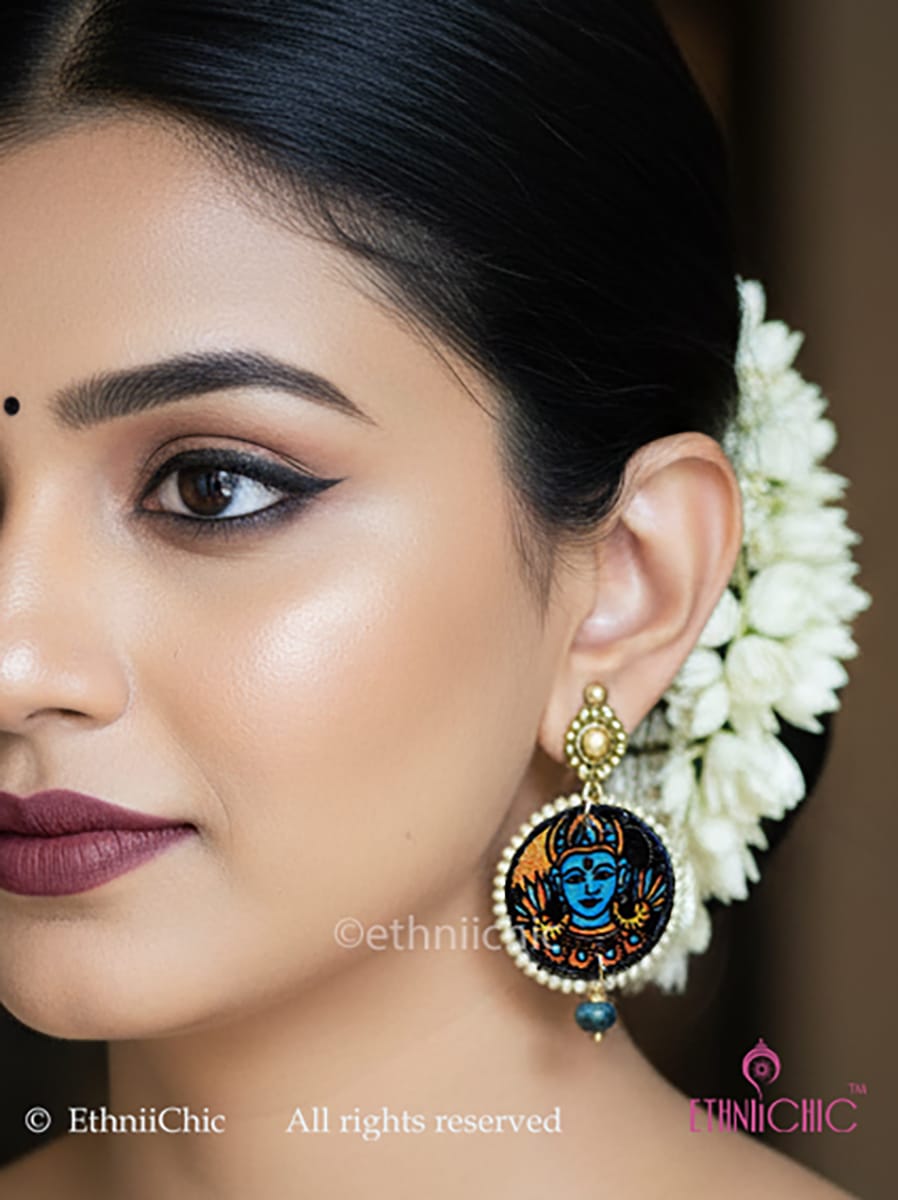 Close-up of a woman wearing earrings with a design of Vishnu face hand-painted in Kerala Mural style with a blurred background