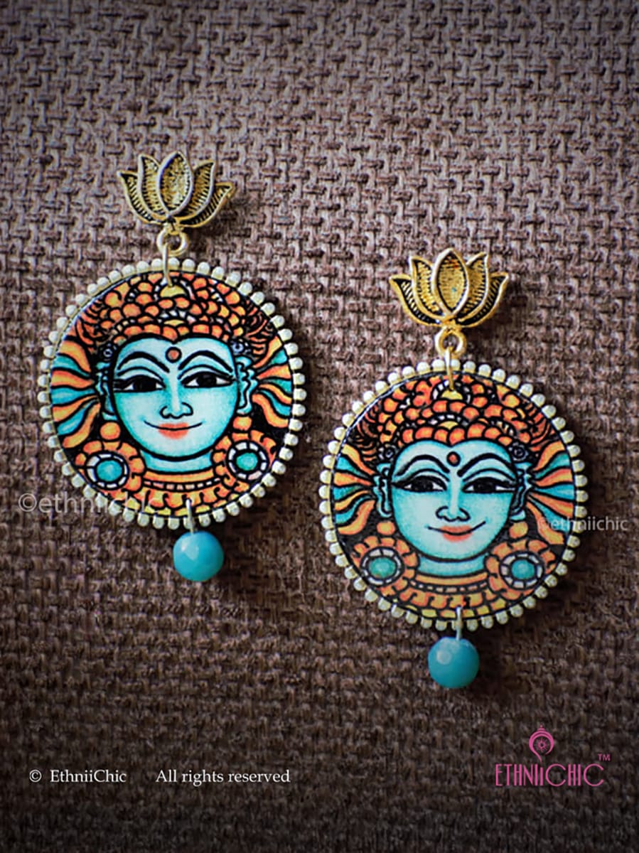 Pair of Kerala Mural Hand-Painted Earrings – Krishna Teal on a brown fabric background